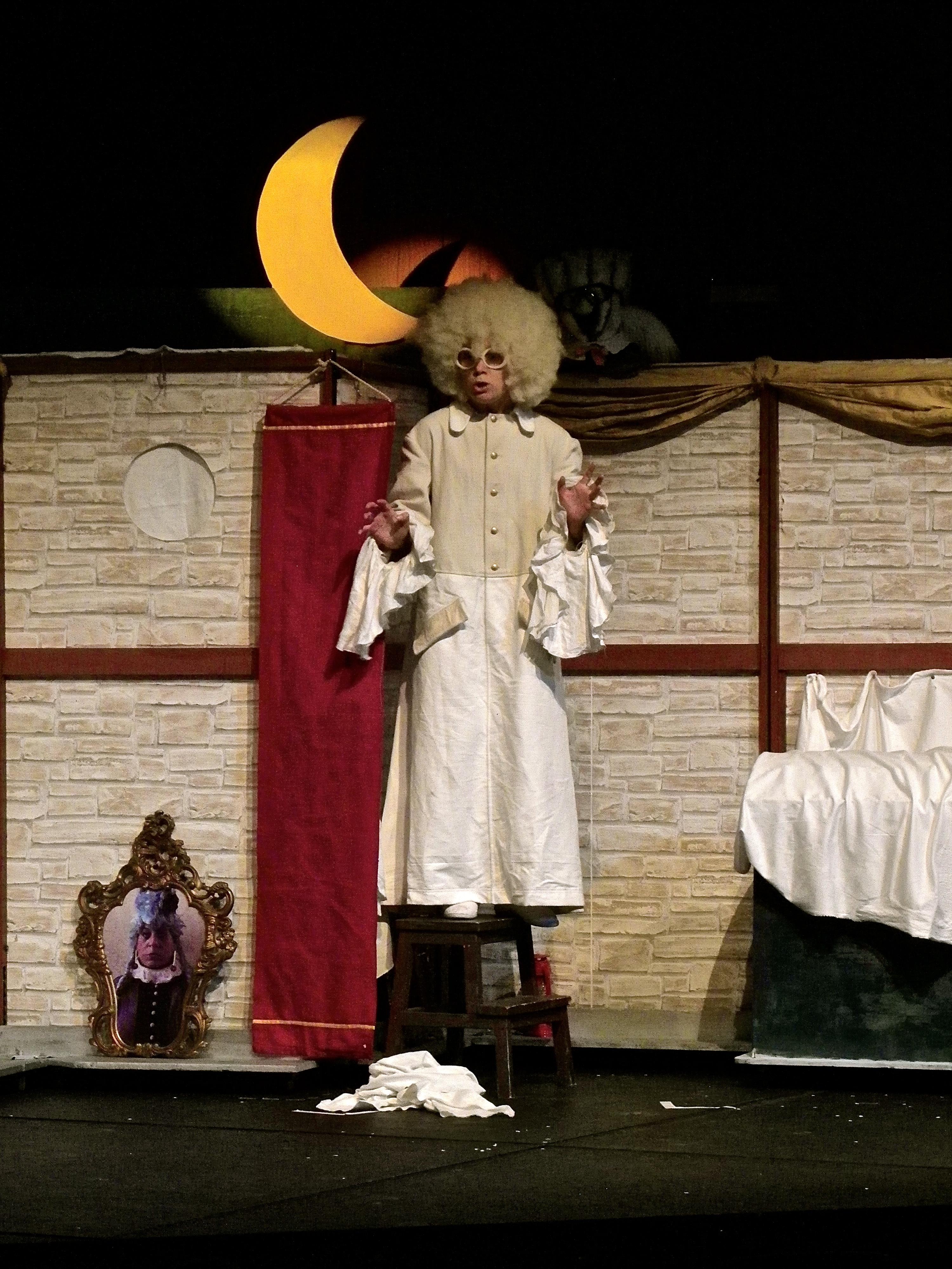 Ein Schauspieler in weißem Gewand steht auf der Bühne unter Mond
